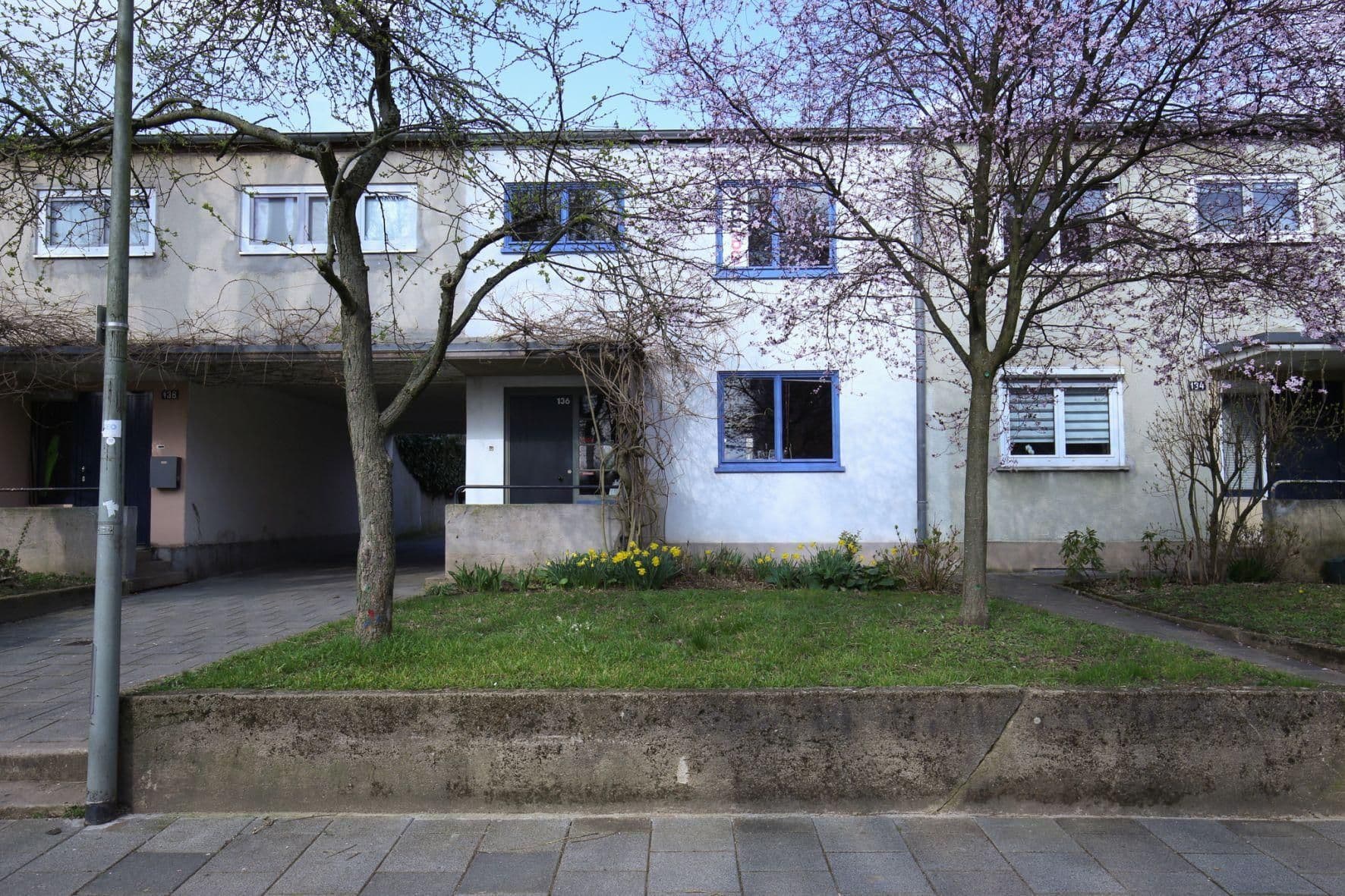 Ein Reihenhaus mit kleinen blauen Fenstern und Bäumen im Vorgarten.