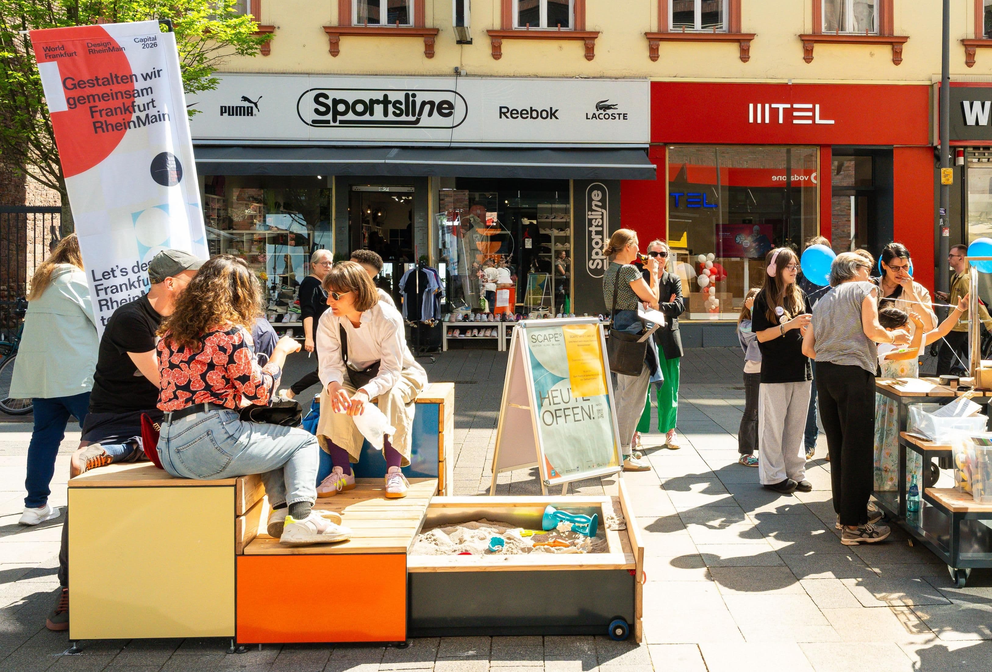 Menschen sitzten auf modularen Möbeln in einer Innenstadt zusammen in der Sonne